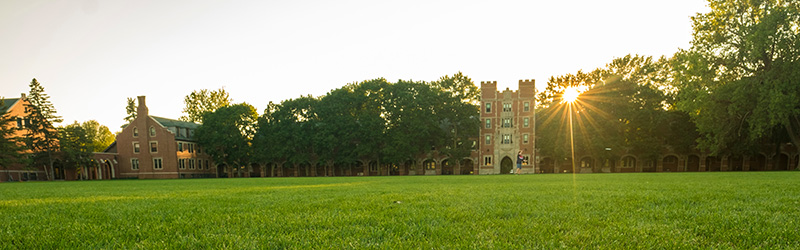 Gates Tower on the campus of Grinnell College. The sun is peaking through the trees which flank the Eastern Side of the tower (Mac Field Side).