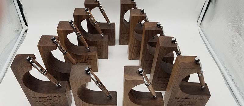 The 2024 Alumni Awards displayed on a table. The awards feature a wooden pen and a wooden holder created using trees removed during the building of the HSSC.