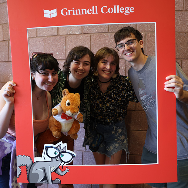 Four students and a stuffed squirrel pose for a photo inside a red frame.