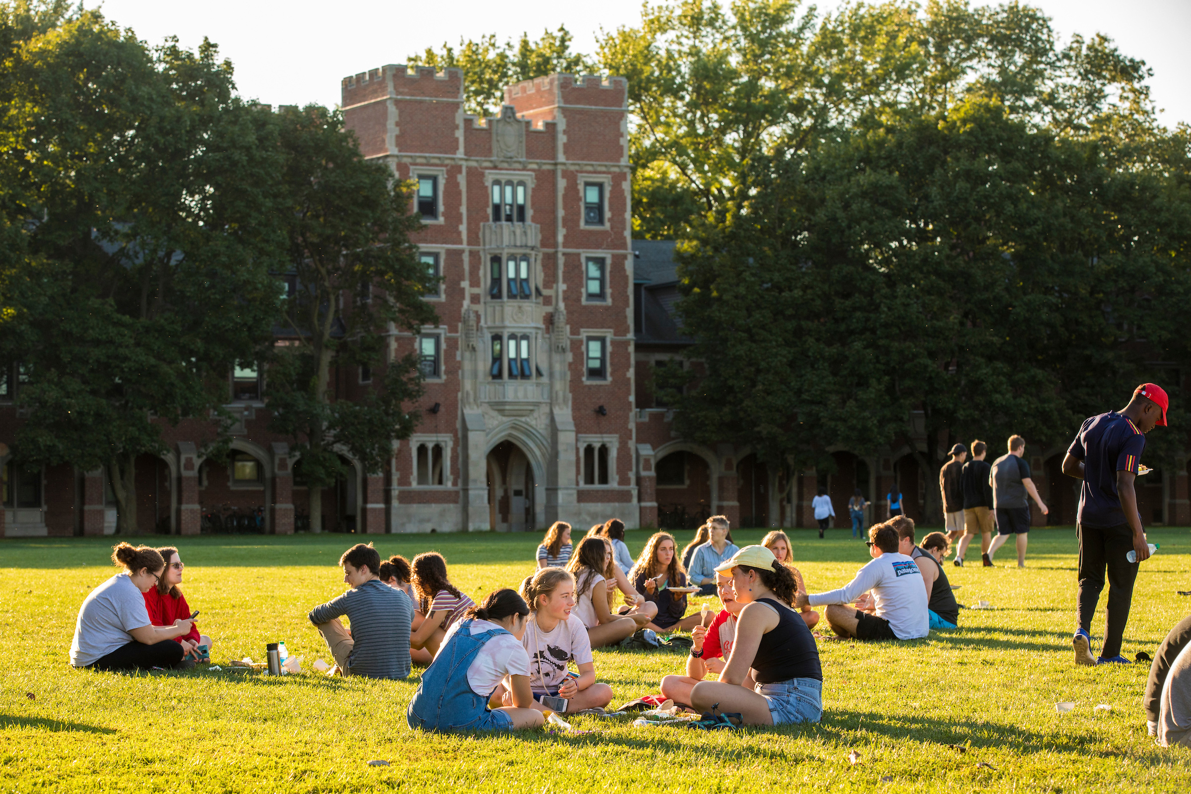 Students sit in Mac Field with Gates Tower in the background