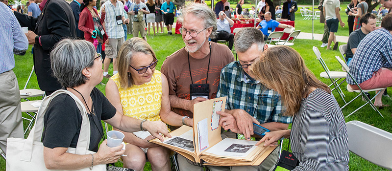 A group of alumni reminisce while looking at an old picture album. 