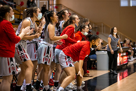 The Pioneer Women's Basketball team look cheer their teammates from the sidelines.