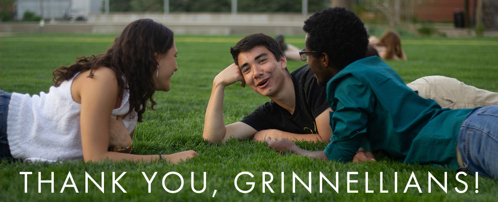 Three students lay on the grass talking and smiling. Text: Thank you, Grinnellians!