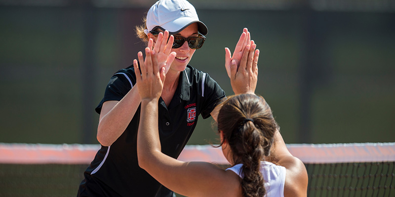 Grinnell women’s tennis coach Paige Madara gives a high-five to a tennis player. 