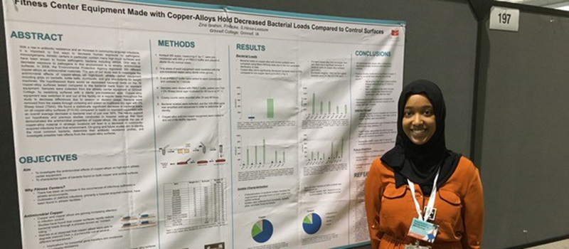 Zina Ibrahim ’17 stands with a presentation exploring using copper as a antibacterial surface.