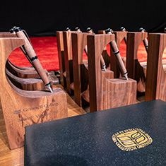 The 2024 Alumni Awards displayed on a table. The awards feature a wooden pen and a wooden holder created using trees removed during the building of the HSSC.