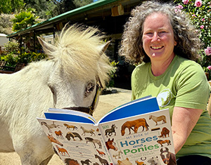 Kendra Hillman Chilcoat &rsquo;94 poses with a horse while reading a horse themed childrens book.