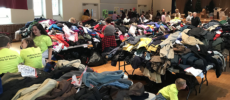 Thousands of coats on several tables in a gym or cafeteria ready for distribution.