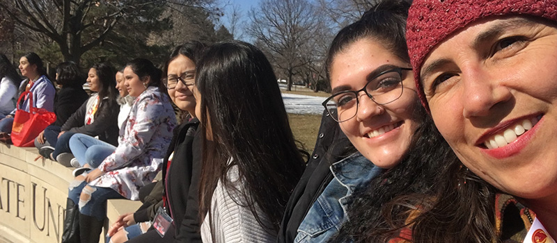 Kristin Stuchis '98 with several Latinx students sitting on top of a Iowa State University sign during a campus visit.