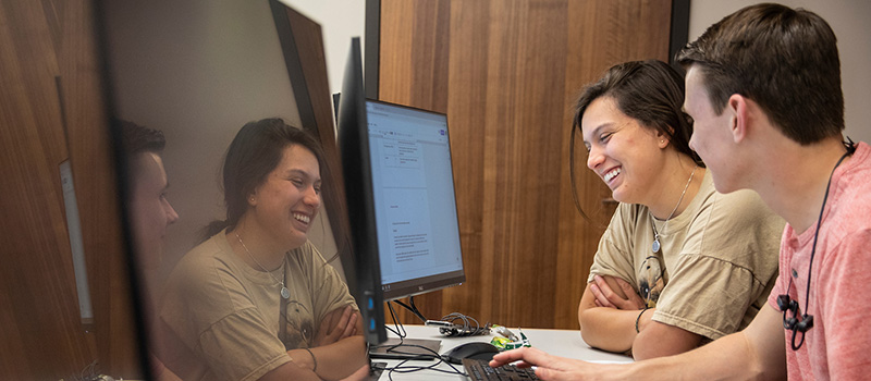 A 2019 photo shows students using computers on the Grinnell College campus. This photo features two students working on a project together and a turned off monitor is reflecting their images.