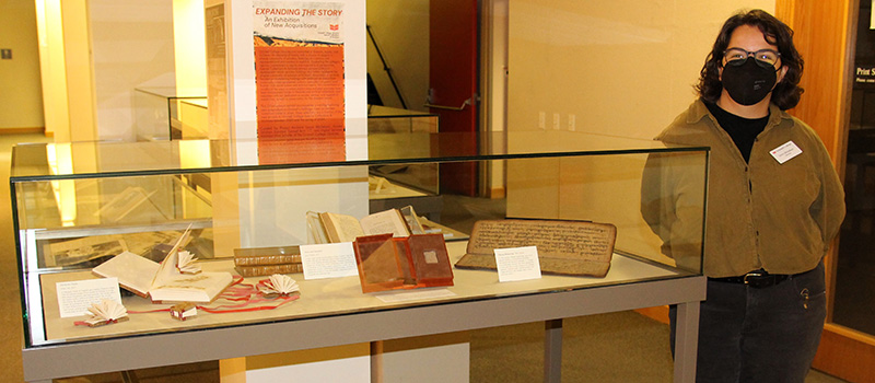 Project Archivist Laura Michelson stands next to the Expanding the Story exhibit in the lowest level of Burling Library.