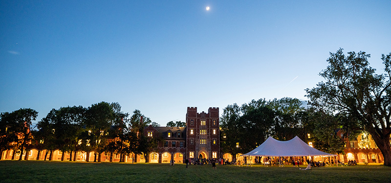 The moon sits over Gates Tower with the loggia illuminated. A tent sits in the foreground on Mac Field.