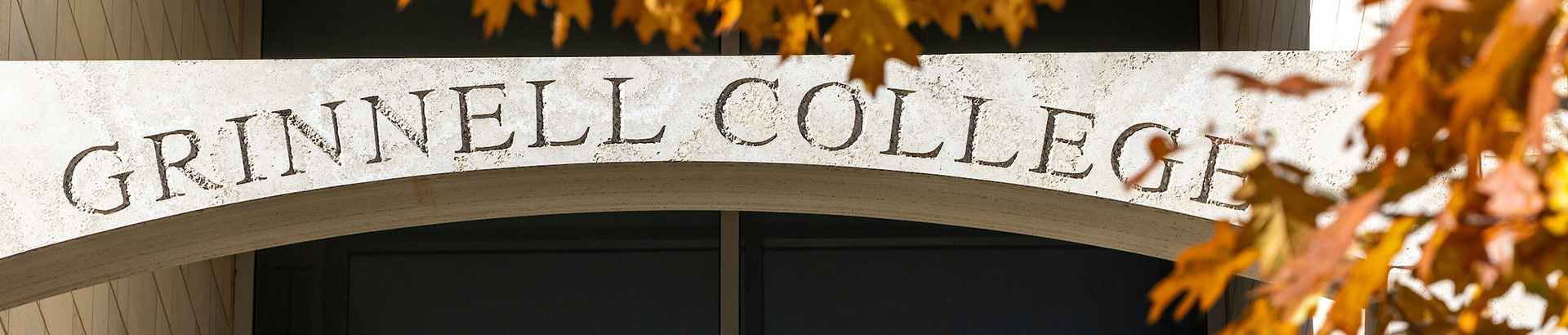 Grinnell College carved into the stone work as part of the Northeast campus dorms. Fall leaves appear in the foreground.