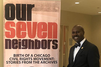 Brian Smith ’94 poses next to a banner for "Our Seven Neighbors," a presentation Brian created. 