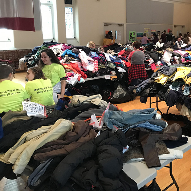 Thousands of coats on several tables in a gym or cafeteria ready for distribution.