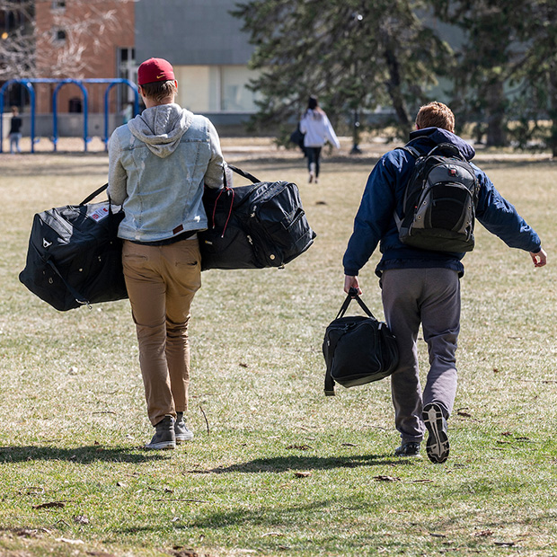 Two students carrying duffle bags walking across Mac Field