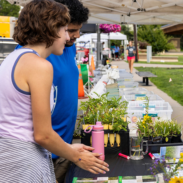 Two students stand next to a table full of plants.