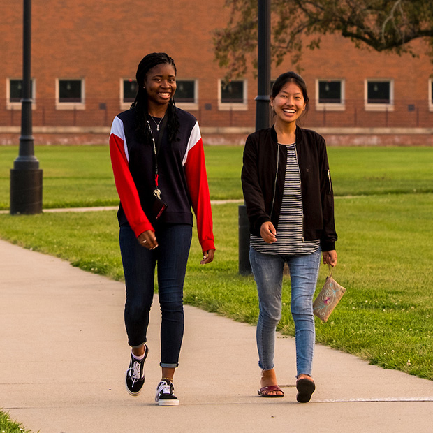Two students walk down a sidewalk on campus.