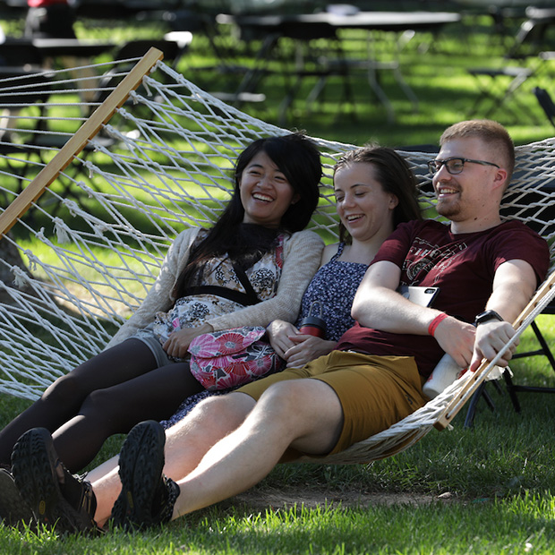 Three alumni sit on a hammock on campus.